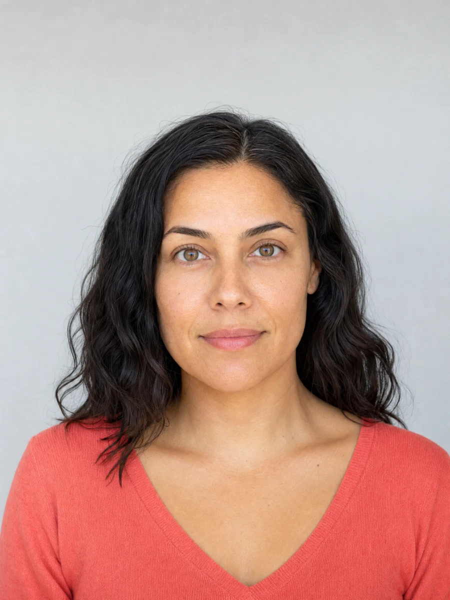 A woman with golden-brown skin, deep brown hair, clear amber-brown eyes and a coral knit top.