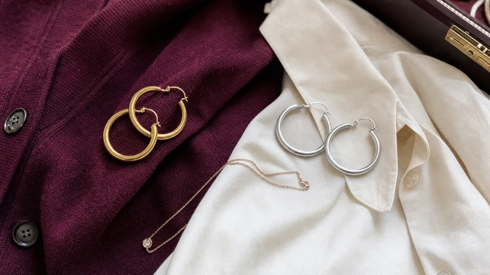 Gold and silver hoop earrings on a burgundy knit and ivory blouse.